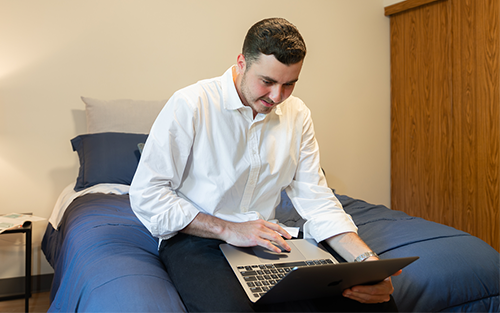 Student sitting on bed with laptop