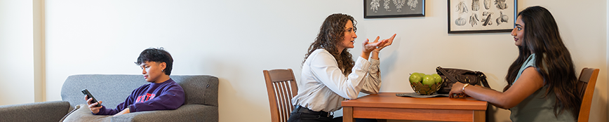 Two students sitting at a kitchen table and one sitting at a couch